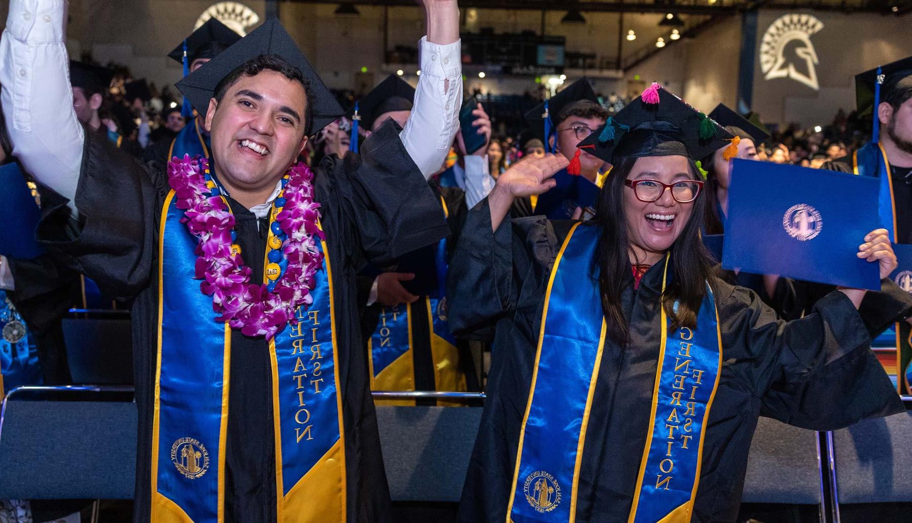 Two graduates pose with their diploma during commencement.