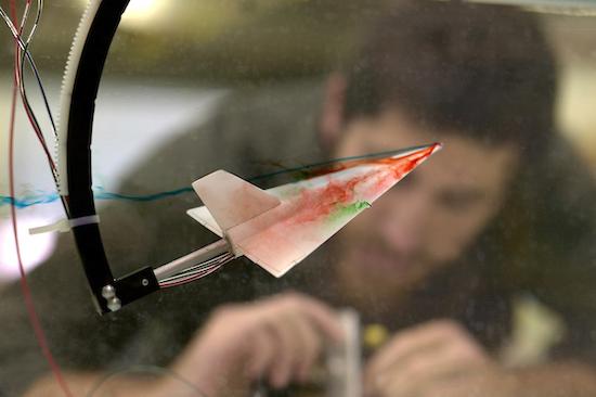 closeup of airplane shape test with colored smoke streaming from wings. blurred person in background